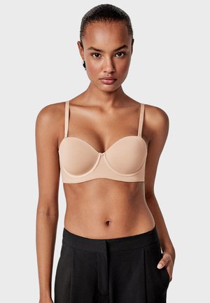 Soutien-gorge en beige doux, doté de bonnets moulés, de fines bretelles réglables et de détails de couture subtils. Le matériau semble lisse et extensible.