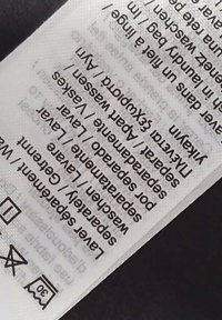Etiqueta de cuidado blanca con texto negro que enumera las instrucciones de lavado. Contiene iconos para el cuidado, lavado por separado y detalles de la tela.