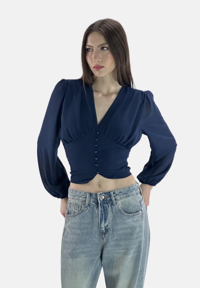 Dunkelblaues Langarmoberteil mit V-Ausschnitt, ausgestattet mit einer knöpfbaren Vorderseite und Raffung, kombiniert mit hellblauen, hochgeschnittenen Jeans.