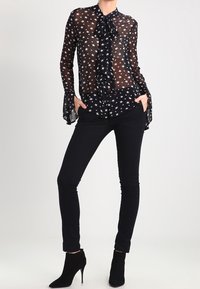 Svart genomskinlig blus med vitt stjärnmönster, med snörning i halsen och utställda ärmar, kombinerad med åtsittande svarta byxor och ankelstövlar.