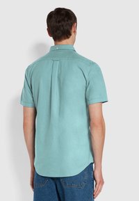 Korte mouwen overhemd in licht teal katoen, met een rugleiste en een afgeronde zoom. Beschikt over een knopenkraag en minimale stikdetails.