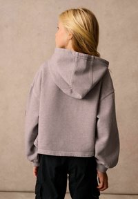 Felpa grigia a maniche lunghe con cappuccio grande, polsini a coste e spalle cadenti, abbinata a pantaloni cargo neri. Design classico e semplice.
