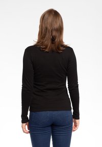 Maglietta nera a maniche lunghe con un design aderente, realizzata in tessuto morbido. Abbinata a jeans blu scuro con un classico stile a cinque tasche.