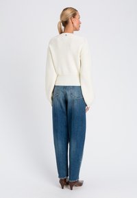 Maglione bianco a coste con un taglio corto, abbinato a jeans blu a vita alta e larghi. Le scarpe a punta marroni completano l'outfit.
