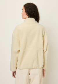 Krémový fleece pulover s vysokým golierom, štruktúrovaným povrchom a voľným strihom. Obsahuje zadný šev a spadnuté ramená.