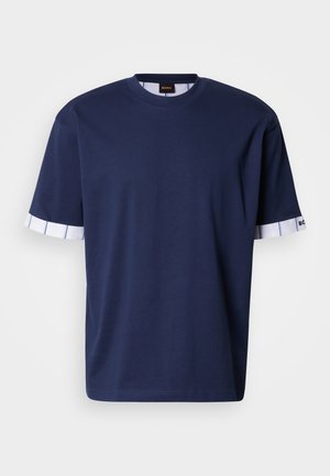 Μπλε ναυτικό βαμβακερό T-shirt με στρογγυλή λαιμόκοψη και κοντά μανίκια. Οι μανσέτες των μανικιών έχουν λευκό ριγέ μοτίβο και λεπτομέρειες με λογότυπο.