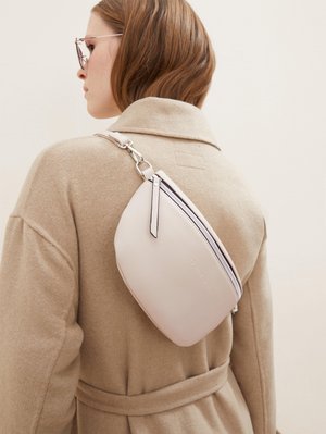 Sac crossbody rose clair avec une surface texturée, fermeture à glissière et une sangle fine, porté sur un manteau beige. Accents en métal argenté.