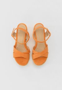 Oransje semskede sandaler med kryssede stropper, en side-spenne og en lav espadrille-lignende kile såle. Glatt indre fôr og behagelig passform.