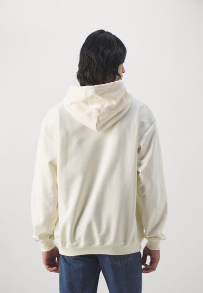 Cremefarvet hoodie med en stor, blød hætte. Har ribbede manchetter og kant, og har en afslappet pasform. Bæres med blå, let figursyede jeans.