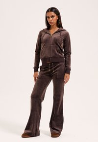 Bruin velours trainingspak met een rits-houthoodie met voorzakken en wijde broekspijpen. Details in goudkleurige hardware maken het ontwerp af.