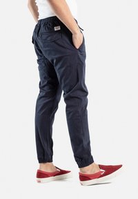 Pantalones cargo azul marino con puños elásticos y bolsillos, hechos de un material suave y texturizado. Combinados con zapatillas rojas tipo slip-on con suelas blancas.