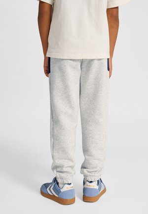 Szare spodnie dresowe z elastycznymi ściągaczami, z ciemnoniebieskimi akcentami po bokach, zestawione z niebieskimi trampkami i jasnym t-shirtem.