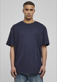 Tricou din bumbac de culoare bleu marin, cu o croială lejeră, decolteu rotund și mâneci scurte; are un design minim și fără logo-uri vizibile.