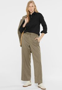 Black button-up shirt, beige glen plaid wide-leg trousers with drawstring, and beige sneakers. Jacket draped over arm for contrast.