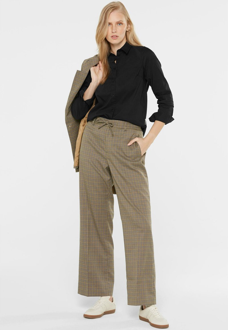 Black button-up shirt, beige glen plaid wide-leg trousers with drawstring, and beige sneakers. Jacket draped over arm for contrast.