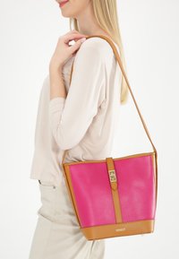 Roze leren handtas met een gestructureerde vorm, bruine accenten, een bovenkant-sluiting en een schouderriem. Getextureerd oppervlak voor grip.