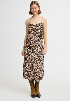 Robe maxi imprimé léopard en tissu léger avec des bretelles spaghetti ; présente une coupe fluide et un subtil éclat ; associée à des bottes de cowboy marron.