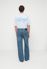 Ανοιχτό μπλε μπλουζάκι με μεγάλο λευκό γραφικό στην πλάτη, σε συνδυασμό με χαλαρά μπλε τζιν παντελόνια με πίσω τσέπες.