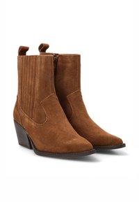Botines de ante marrón con puntera afilada, tacón bajo apilado, paneles elásticos en los laterales y cierre de cremallera. El acabado texturizado complementa el diseño.