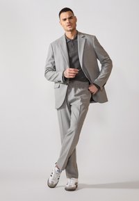 Helles graues Anzug-Outfit mit einem strukturierten grauen Poloshirt, kombiniert mit weißen und grauen Sneakers. Der Anzug hat eine taillierte Passform und eine Hose mit Kordelzug.