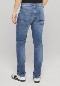 Blaue Jeans aus Denim mit schmaler Passform, ausgestattet mit zwei Gesäßtaschen mit einem dezenten Muster, getragen mit weißen und schwarzen Sneakern.