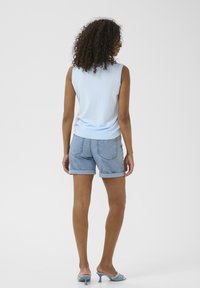 Haut sans manches bleu clair associé à un short en jean avec un ourlet retroussé. Le look est complété par des sandales à talons bleues.