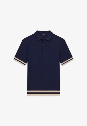 Granatowa koszulka polo z krótkimi rękawami, trzyczęściowym rozcięciem na guziki i beżowymi podwójnymi paskami na krawędziach rękawów i dolnej części.