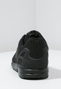 Black athletic shoe featuring a breathable mesh upper, cushioned sole, enhancing comfort. Rear design includes textured accents and logo detail.