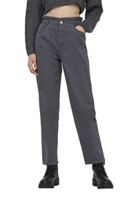 Pantaloni in denim grigio con vestibilità rilassata, elastico in vita e tasche laterali, abbinati a stivali neri con lacci spessi.