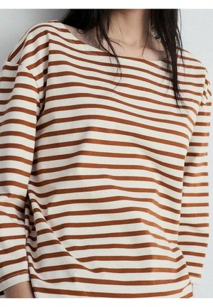 Personne portant un t-shirt à manches longues rayé horizontalement marron et blanc avec un col large.