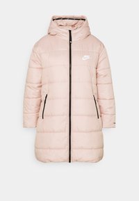 Ljust rosa vadderad Nike vinterjacka med huva, framdragkedja, sidofickor och vit logotyp på bröstet mot en neutral bakgrund.