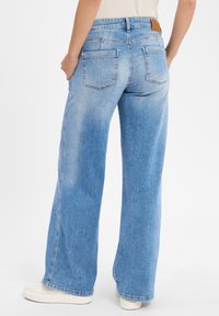 Hoge taille, wijde jeans in lichtblauwe denim. Bevat twee achterzakken en een bruine leren label op de tailleband. Soepele textuur.
