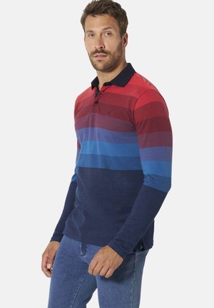 Man wearing a long-sleeve polo shirt with horizontal stripes in red, purple, blue, and navy, paired with blue jeans, against a white background.