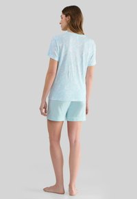 Conjunto de pijama azul claro que incluye una camiseta de manga corta con un patrón de hojas y pantalones cortos a juego de color sólido. Tejido suave y transpirable.