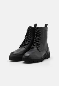 Bottines noires en cuir avec une finition lisse, bout rond, fermeture à lacets à l'avant et semelle en caoutchouc robuste. Elles disposent d'une languette à l'arrière.