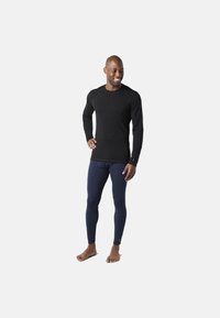 Langærmet sort top og marineblå leggings lavet af glat stof, med et tætsiddende design, uden synlige mønstre eller hardware.