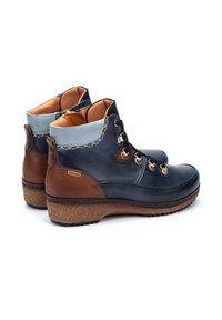 Botas de tobillo bicolor con parte superior de cuero azul oscuro, acentos texturizados marrones, hardware dorado y una suela de textura similar al corcho.
