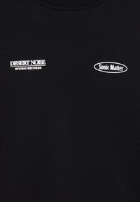 Tissu noir avec logos en texte blanc, « DESERT NOISE STUDIO RECORDS » à gauche et « Sonic Matter » dans un ovale à droite.