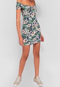 Sukienka w kwiaty, bez ramiączek, w granatowym kolorze z zielonymi liśćmi i różowymi kwiatami. Dopasowany krój, krótka długość, połączona z beżowymi sneakersami.