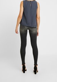 Ärmlös marinblå blus med en texturerad halsringning, i kombination med svarta skinny jeans. Jeansen har en urtvättad design och bakfickor.