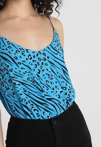 Blå linne med svart leopard- och zebramönster. Tunnaxlade band och lös passform, kombinerat med svarta byxor med hög midja.