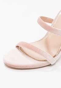 Vaaleanpunaiset samettiset korkeat sandaalit, joissa on kaksi kapeaa nauhaa ja sileä, vaalean värinen pohja, jossa on hieno kiilto.