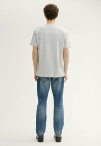Camiseta de algodón gris con cuello redondo, mangas cortas, combinada con unos pantalones vaqueros de mezclilla azul con un acabado desgastado y corte recto.