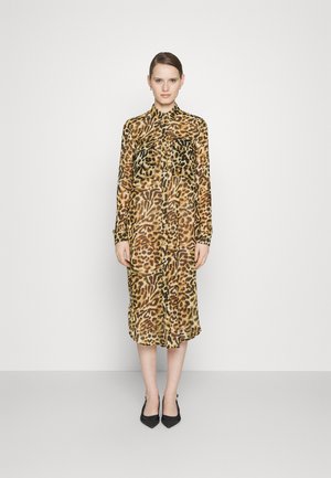 Priehľadné šaty s leopardím vzorom v odtieňoch hnedej a čiernej farby, s golierom, dlhými rukávmi a gombíkmi vpredu. Zvýraznené dvoma náprsnými vreckami.