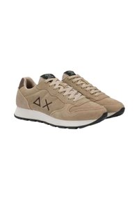 Baskets en velours beige avec une semelle en caoutchouc blanc, présentant un design à lacets et un logo géométrique marron sur le côté. Surface texturée et accents contrastés.