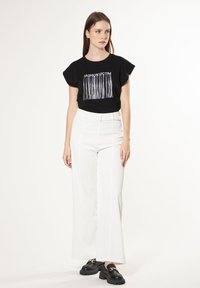 Camiseta de algodón negra con gráfico de "FASHION VICTIM", combinada con pantalones de pierna ancha blancos de cintura alta y mocasines negros gruesos.