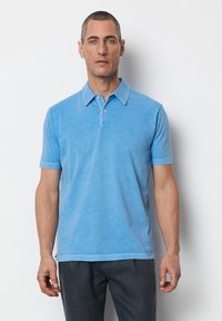 Hellblaues Polohemd aus weicher Baumwolle, mit klassischem Kragen, kurzen Ärmeln und einer Knopfleiste mit drei Knöpfen. Glatte Textur.