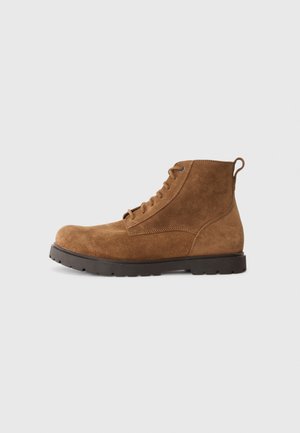 Stivaletti in suede marrone con punta arrotondata, lacci sulla parte anteriore e linguetta sul retro. Superficie testurizzata e suola in gomma resistente.
