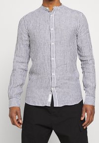 Lange mouwenshirt van zacht materiaal met zwarte en witte verticale strepen, een mandarin col, en knoopsluiting.