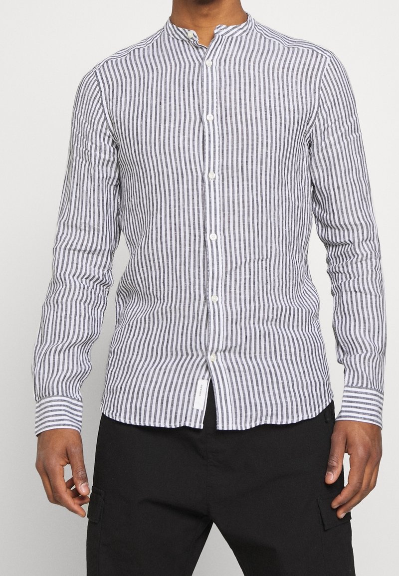 Lange mouwenshirt van zacht materiaal met zwarte en witte verticale strepen, een mandarin col, en knoopsluiting.